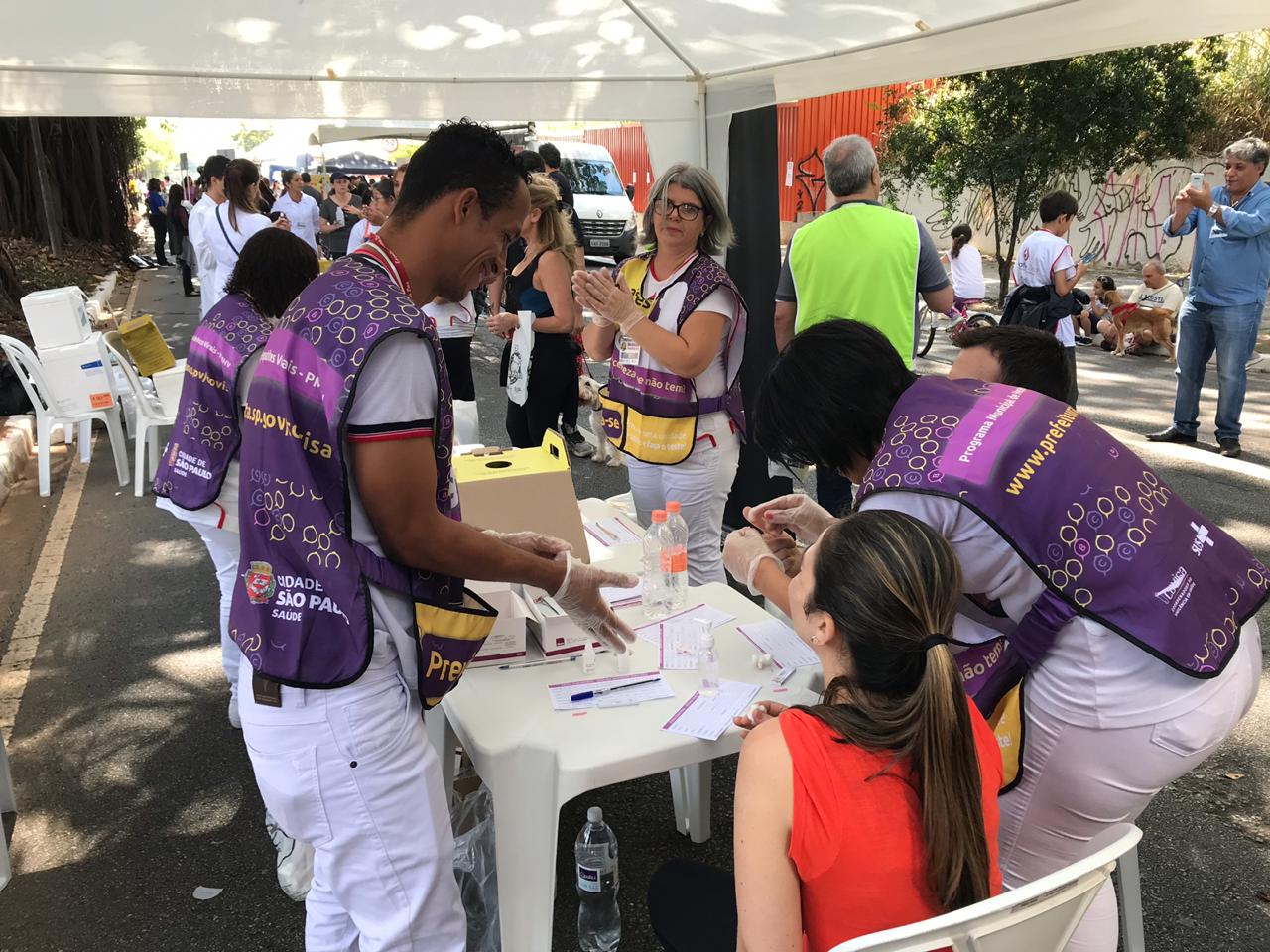 Momento da vacinação humana durante o evento. Profissionais da saúde são identificados na foto por um jaleco na cor roxa 